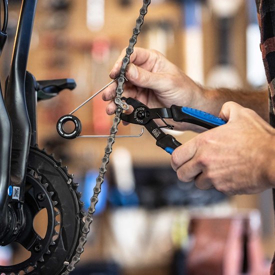 Une personne utilise une pince à chaîne noire avec poignées bleues pour monter une chaîne de vélo.