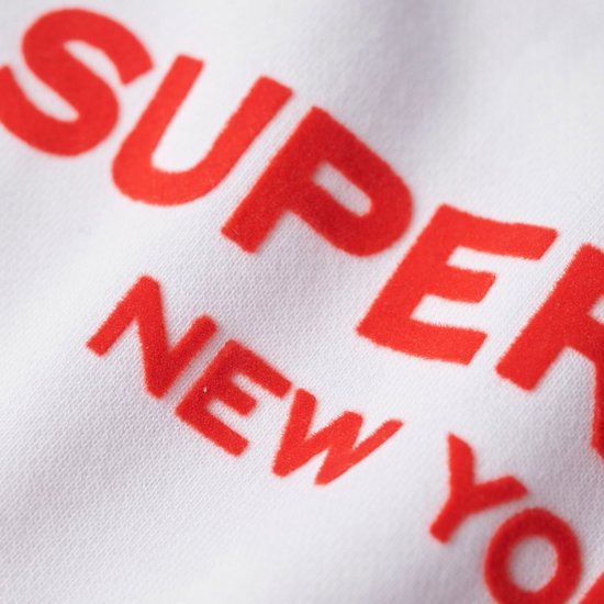 Gros plan de l'inscription rouge 'SUPERDRY NEW YORK' sur un sweat blanc.