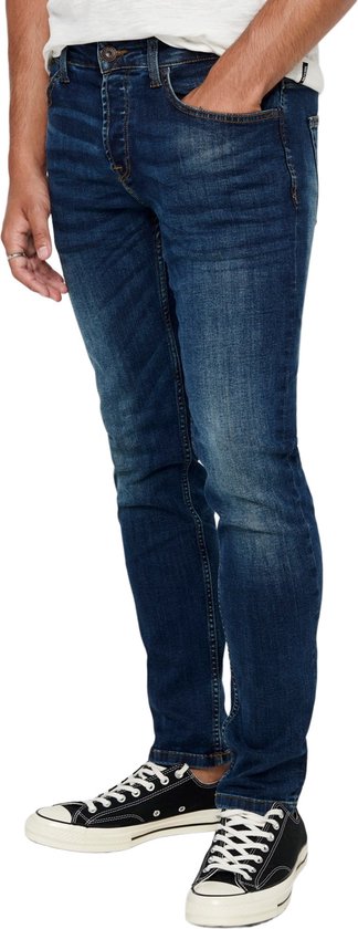 Zijaanzicht van een man in een donkerblauwe skinny jeans met slijtageplekken.