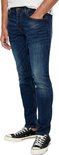 Zijaanzicht van een man in een donkerblauwe skinny jeans met slijtageplekken.