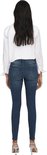 Model in een donkerblauwe skinny jeans met lichte slijtageplekken en een witte blouse.