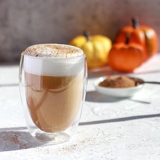 Verre à double paroi rempli de lattes à la citrouille, garni de mousse de lait et de cannelle.