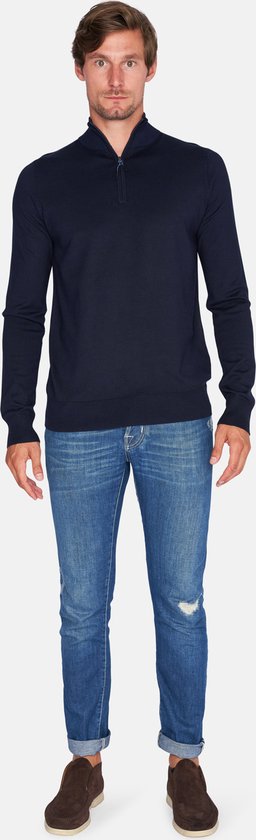 Man in donkerblauwe trui met rits tot de borst en jeans.