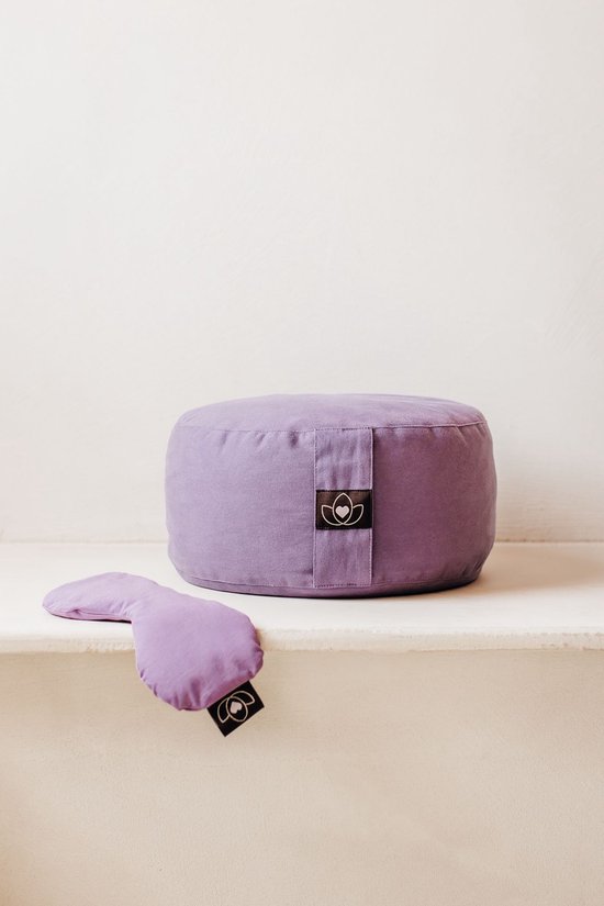 Coussin de méditation violet avec un masque pour les yeux violet à côté.