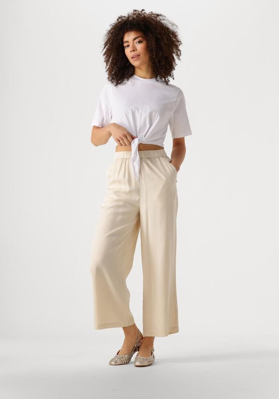 Model met krullend haar in een witte crop top en crème wijde culotte broek met elastische tailleband.