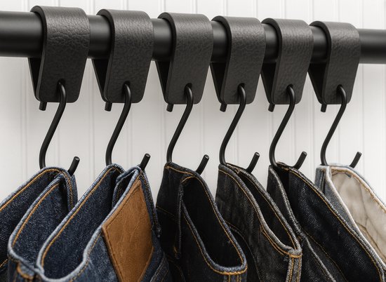 Zwarte leren lussen met metalen S-haken, waaraan meerdere spijkerbroeken hangen.