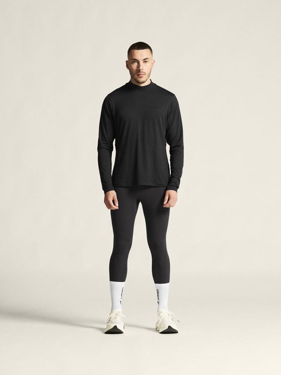 Man van voren gezien in een zwarte longsleeve en zwarte sportlegging. Draagt witte sokken en sneakers.