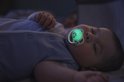 Baby slaapt met een gloeiende, lichtgroene Philips Avent Ultra Air fopspeen met libelpatroon.