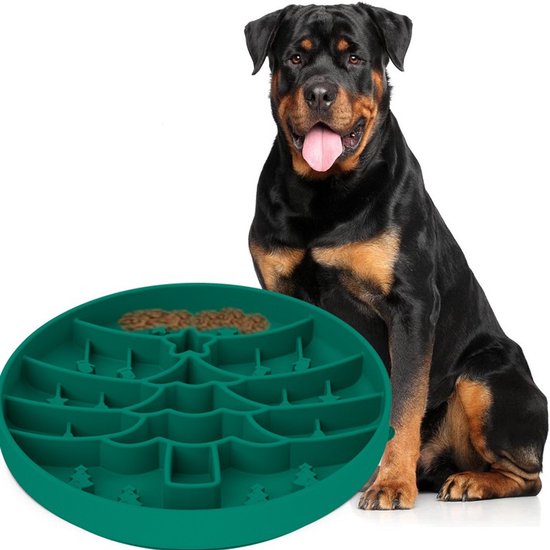 Een Rottweiler zit naast een groene voerbak met boomvormig labyrint, gevuld met brokken.