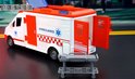 Wit ambulance speelgoed met rode deuren, met een brancard ernaast. De achterdeuren zijn open.