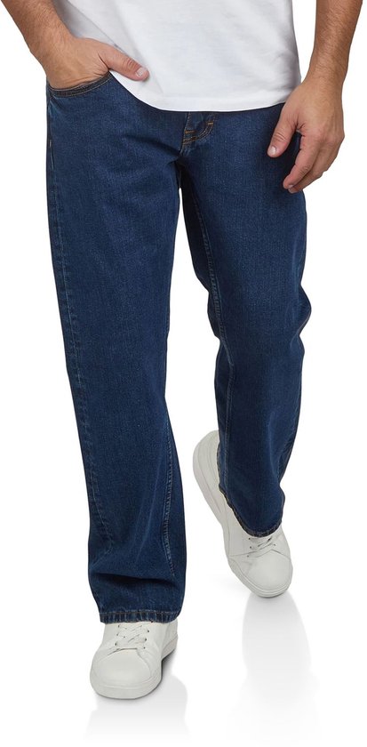 Man van voren in een donkerblauwe bootcut jeans met oranje stiksels en witte sneakers.