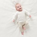 Baby in een wit gebreid vestje met omslagsluiting, liggend op een witte sprei.