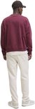 Man in crème joggingbroek en bordeaux hoodie, van achteren gezien.