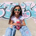 Lachend meisje met zonnebril houdt een rode drinkfles met vogels en regenboog vast, zittend voor graffiti.