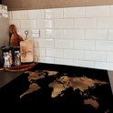Zwarte inductiebeschermer met bronzen wereldkaart, op een aanrecht naast keukengerei.