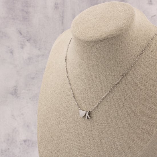 Collier argenté avec un cœur et la lettre K, porté sur un mannequin.