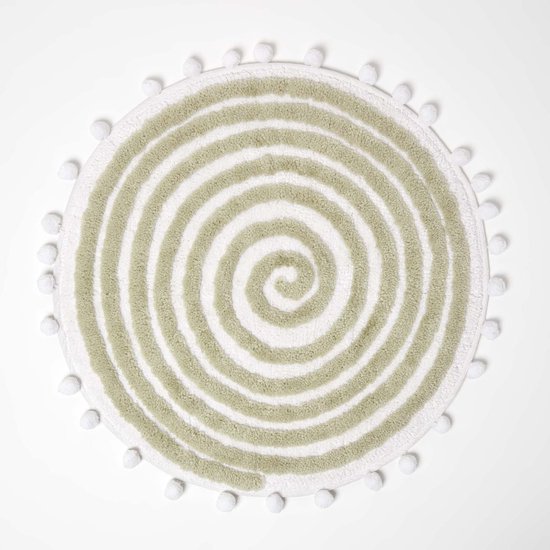 Ronde, saliegroene badmat met spiraalpatroon en decoratieve witte pompons aan de rand.