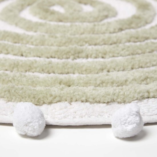 Detail van de ronde, saliegroene badmat met witte pompons en zachte textuur.
