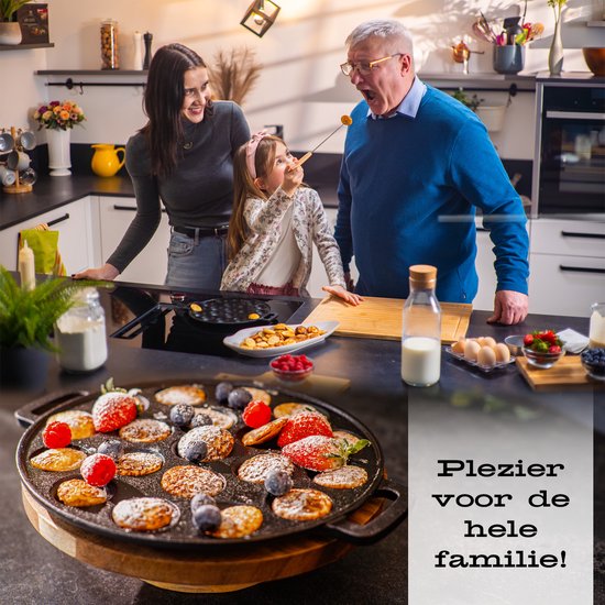 Een man, vrouw en meisje maken pannenkoekjes in een keuken. De pan met poffertjes staat op de voorgrond.