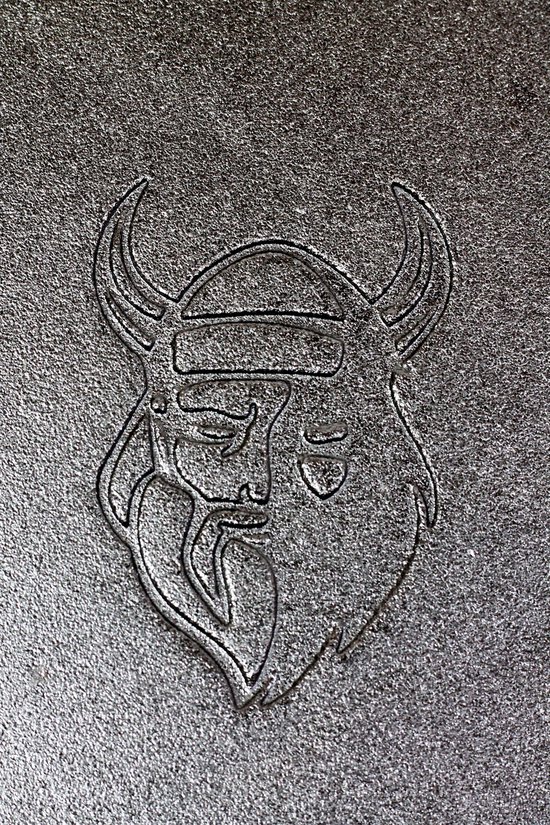 Close-up van een gedetailleerd reliëf van een Viking-hoofd met hoorns op een ruw, gegoten oppervlak.