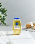 Een gele fles NIVEA Rich Care Shower Oil staat op een witte ondergrond, naast een badborstel en een witte handdoek.