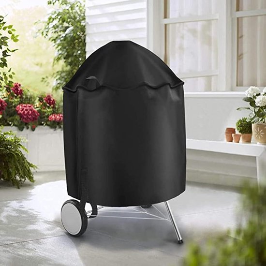 Zwarte, ronde barbecuehoes op wieltjes, in een tuin met bloemen en meubilair.