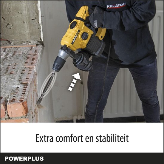 Een persoon in zwarte kleding met een gele Powerplus klopboormachine, demonteert een muur.