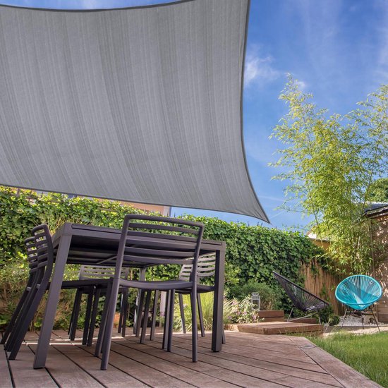Grijze rechthoekige luifel boven een tuintafel, in een tuin met groen en een blauwe stoel.