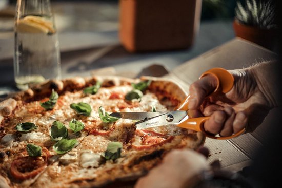 Oranje Fiskars schaar snijdt in een pizza.