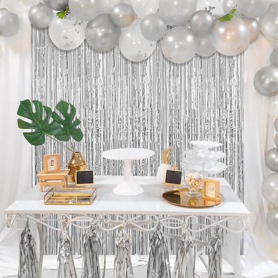 Zilveren glitter gordijn achter feesttafel met ballonnen en planten.