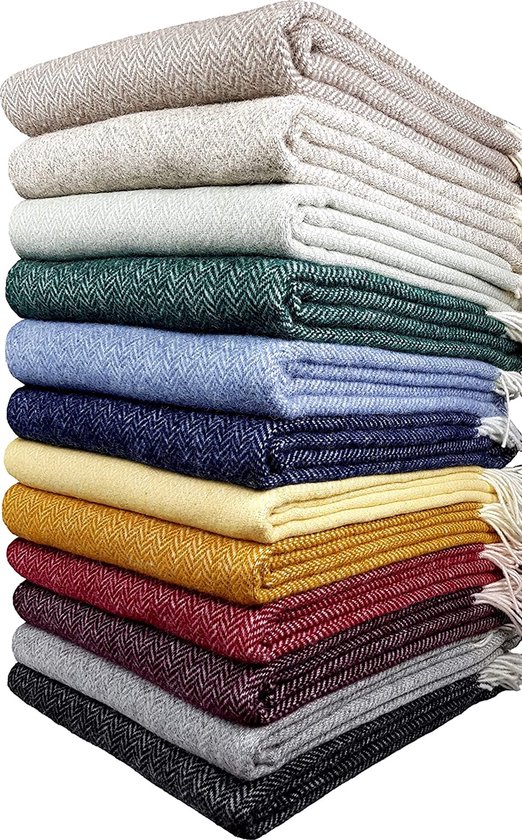 Stapel van wollen plaids in diverse kleuren: beige, groen, lichtblauw, donkerblauw, geel, mosterdgeel, bordeauxrood, grijs en zwart.