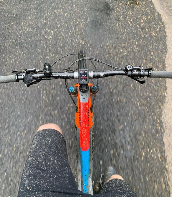 Bovenaf op een mountainbiker tijdens het rijden, met een oranje en blauw frame, stuur en een zwarte fietsbel.
