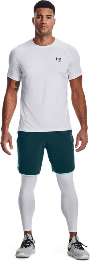 Man draagt witte korte mouwen sportshirt en witte sportlegging met blauw/groene shorts.