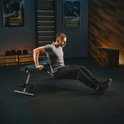 Man in grijs shirt doet een dips oefening op de zijkant van een zwarte fitnessbank.