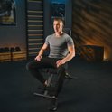 Man in grijs shirt zit op een zwarte fitnessbank met zwarte trainingsbroek.