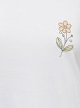 Detail van een kleine geborduurde bloem op een wit t-shirt.
