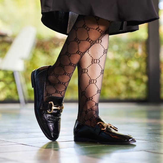 Mocassin vernis noir avec boucle dorée sur une femme portant un collant noir à logos BD.