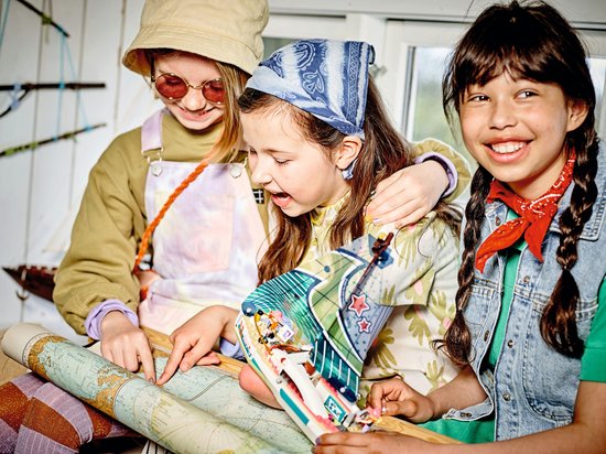 Drie meisjes met hoeden, zonnebrillen en bandanas die naar een kaart kijken en een zeilboot vasthouden.