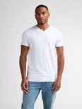 Man met korte zwarte haren, met baardje, draagt een wit T-shirt met V-hals en spijkerbroek.