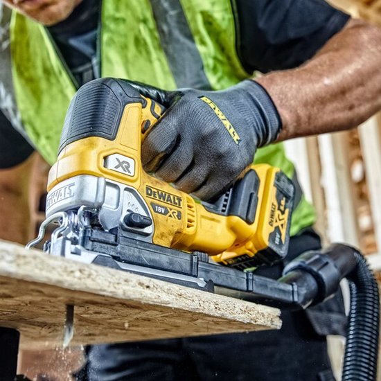 Een bouwmedewerker met een gele en groene veiligheidshes, snijdt in een houten plank met een DeWalt decoupeerzaag.