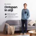 Man met een blauwe pyjamaset met lange mouwen, donkerblauwe borstzak en donkerblauwe broek, zittend op een bank.