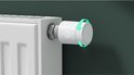 Witte slimme radiatorthermostaat met draairing en digitaal display waarop 23 graden wordt weergegeven, bevestigd aan een witte radiator.