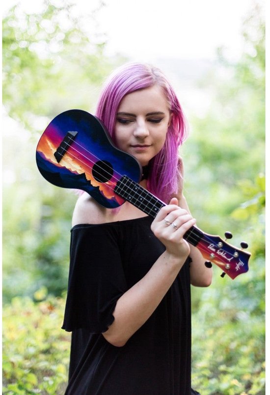 Vrouw met paars haar draagt een ukelele met zonsondergangprint over haar schouder. De ukelele toont blauwe, paarse en oranje kleuren.