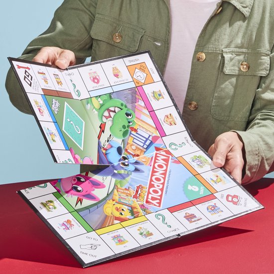 Iemand houdt het Monopoly Junior bordspel open, met een dinosaurus en een hond op het bord.