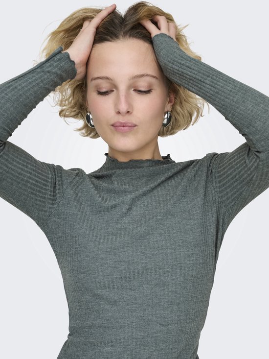 Groene coltrui met lange mouwen, gedragen door een vrouw met blond haar die haar handen door haar haar haalt.