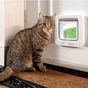 Bruine kattenluik in een deuropening naast een zittende cyperkat. Merk SureFlap.