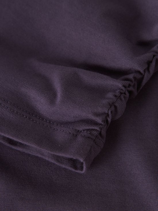 Detail van paarse stof met gerimpelde zoom en stiksels.