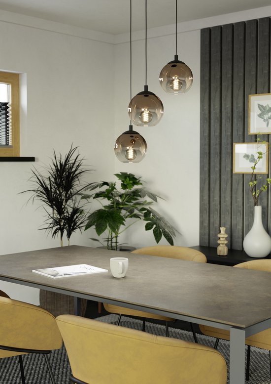 Trois suspensions avec des sphères rondes en verre coloré au-dessus d'une table à manger avec des chaises jaunes.
