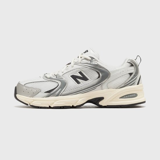 Zijzicht van witte New Balance 530 sneakers met zilveren overlays, zwarte 'N' en crèmekleurige zool.