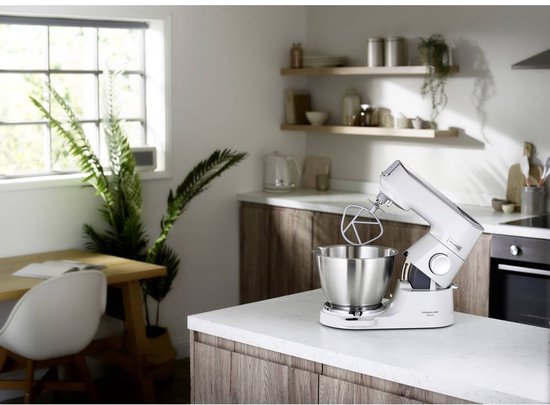 Robot pâtissier Kenwood blanc avec bol inox et feuille, dans une cuisine moderne.